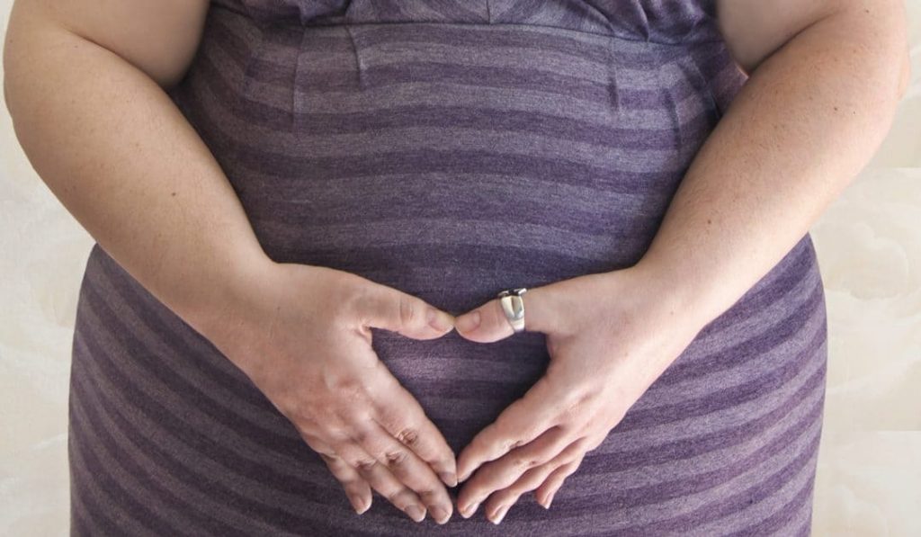 کاهش وزن قبل از بارداری - تصویر خانم بارداری که دستان خود را در حالت ایستاده روی شکمش قرار داده است