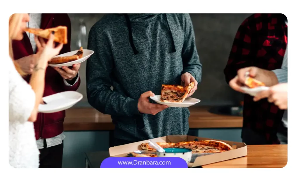 تعدادی مرد و زن که به صورت ایستاده در حال خوردن پیتزا هستند